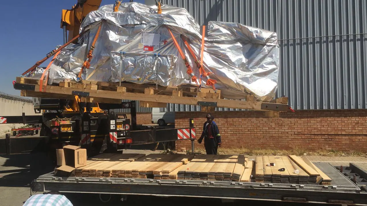 Wrapped machine module being lifted from transport